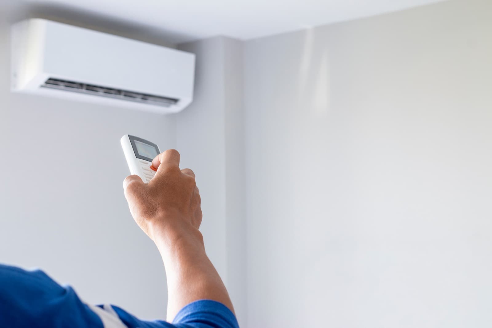 Main qui pointe une télécommande vers un climatiseur mural