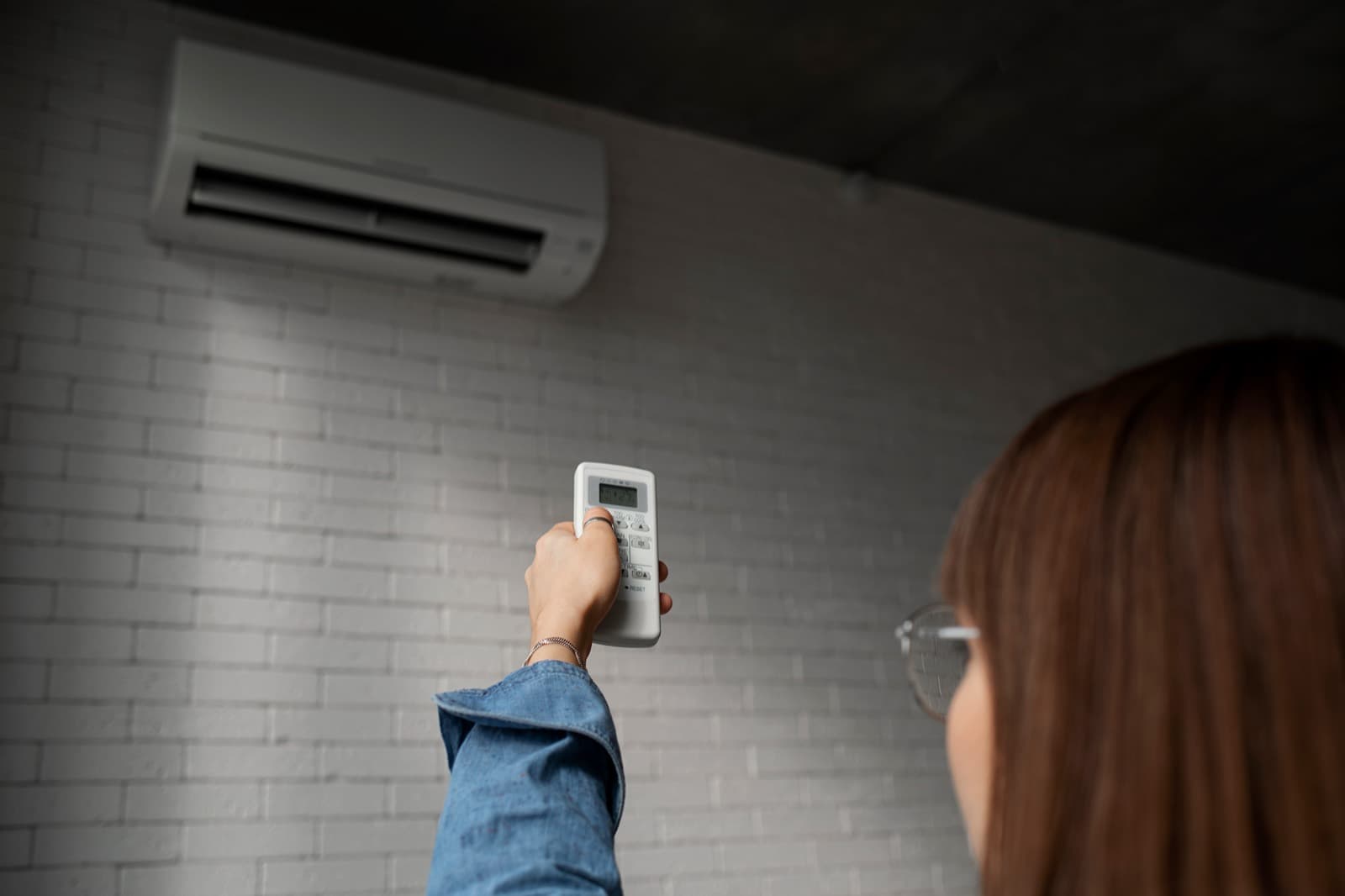 Femme qui règle son climatiseur mural avec la télécommande